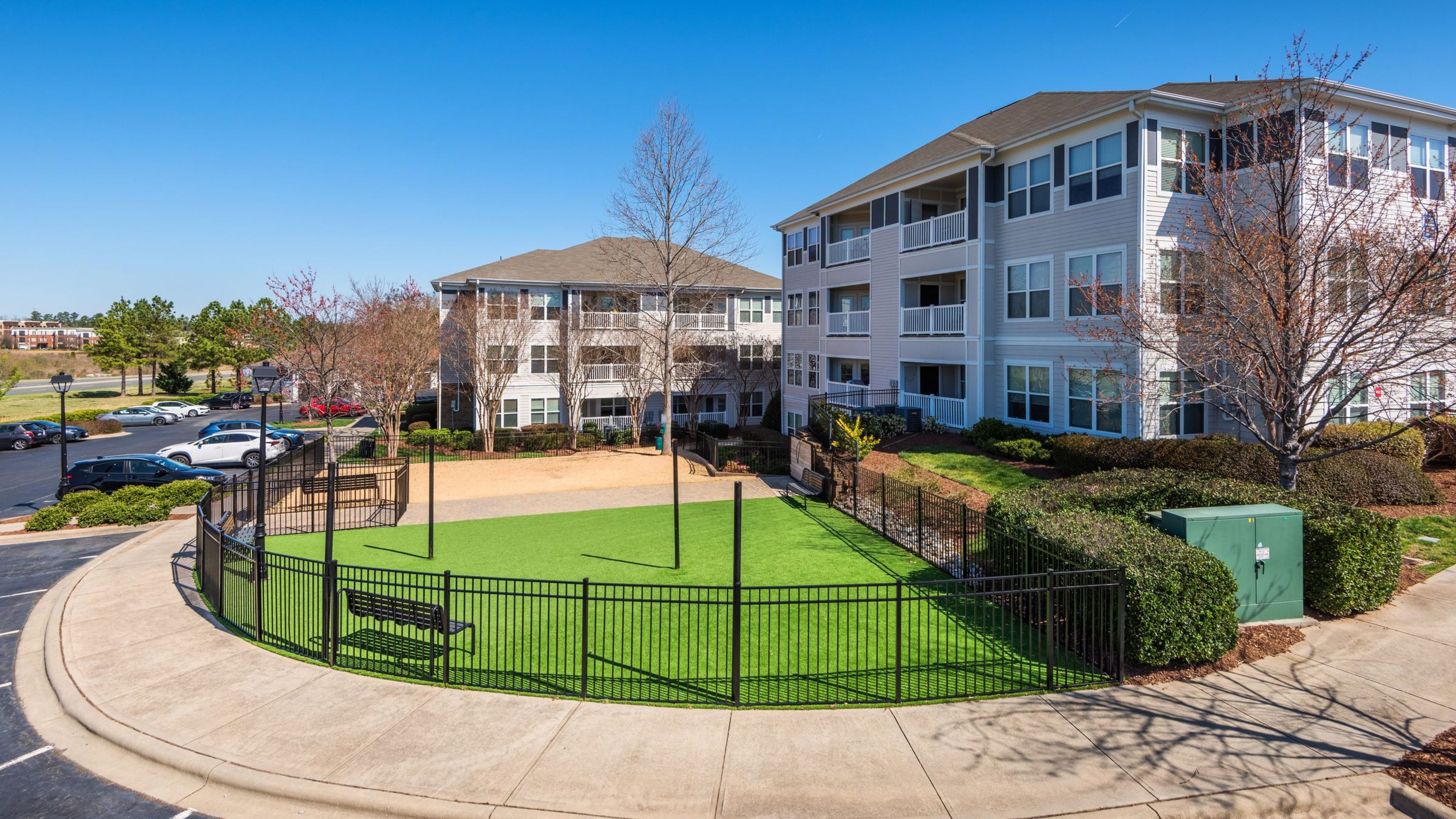 Hawthorne Davis Park apartments community exterior with fenced-in large green lawn on one side, and sandy lot on the other side for dogs